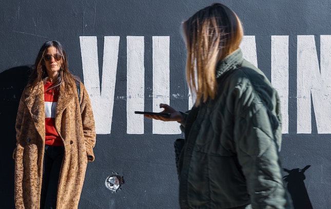 woman standing in front of a wall painted with the word villain