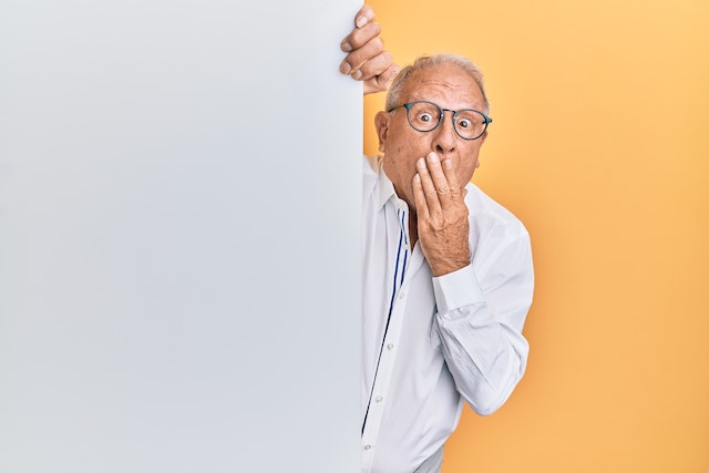 surprised man clutching white board with yellow background