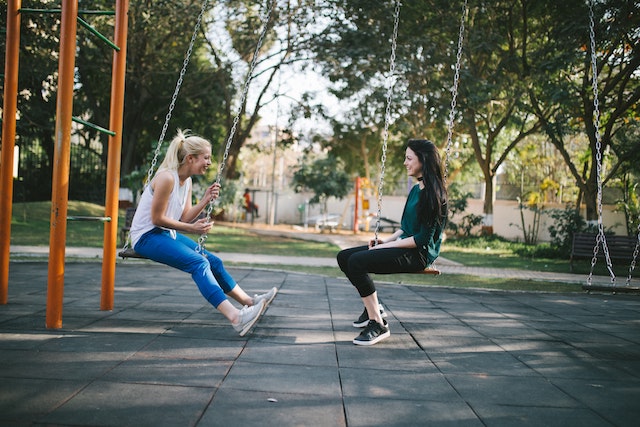 two women on children's swing set talking