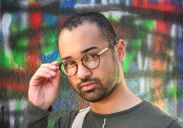 man adjusting glasses in front of graffitti wall