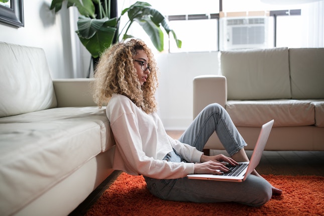 woman sitting on floor in living room working on computer