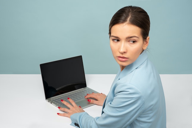 woman using laptop and looking behind as she is acts as a villain