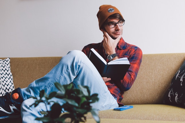 man sitting on a couch considering what he has just read in the book in his hand