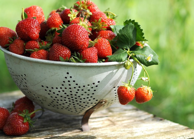 A colander full of fresh strawberries on a wooden table