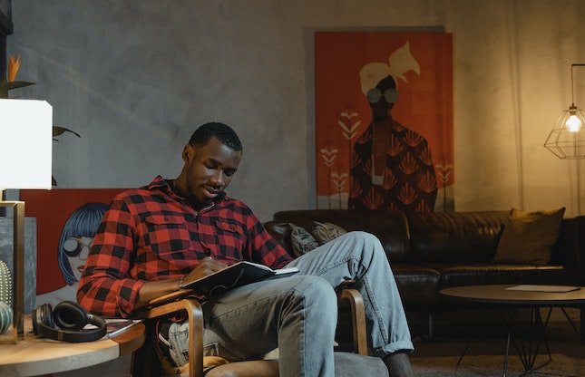 man draped in chair reading a book