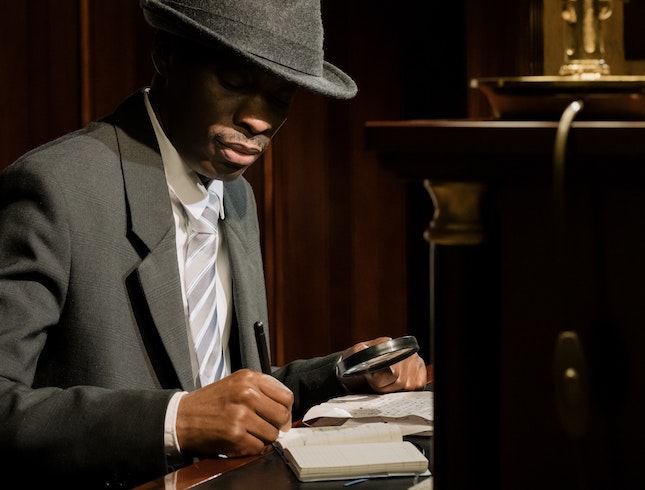 man at desk examining clues with a magnifying glass