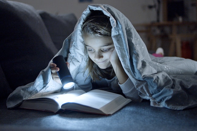 girl involved in storytelling by reading by flashlight under the bed covers