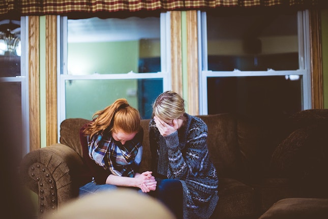 two women crying together in a living room illustrating personal conflict