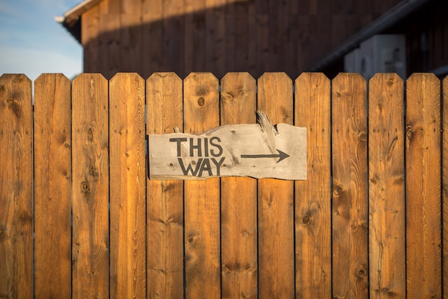 wooden fence with hand lettered sign reading this way with an arrow