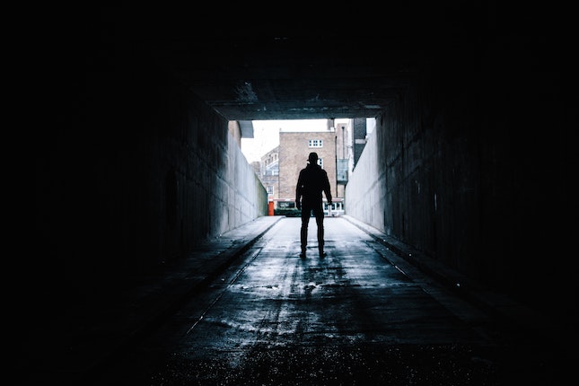 man walking out of a dark tunnel into an unknown area with buildings
