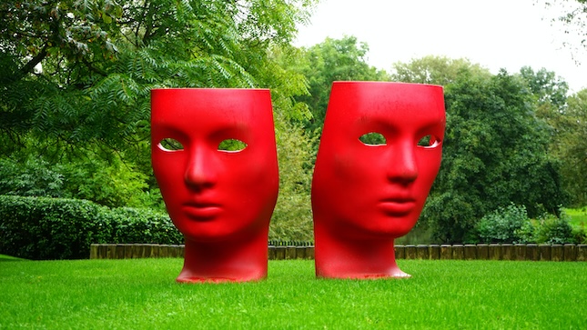 two red mask sculptures in a park