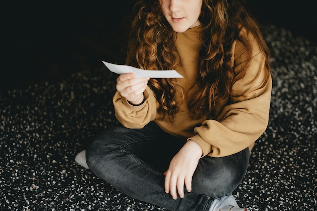 woman sitting cross-legged on the ground reading a mysterious note held in her hand
