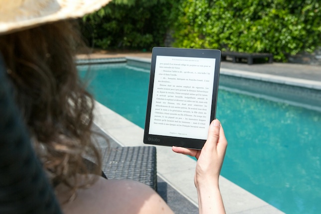 tablet wtih text held by woman sitting by swimming pool